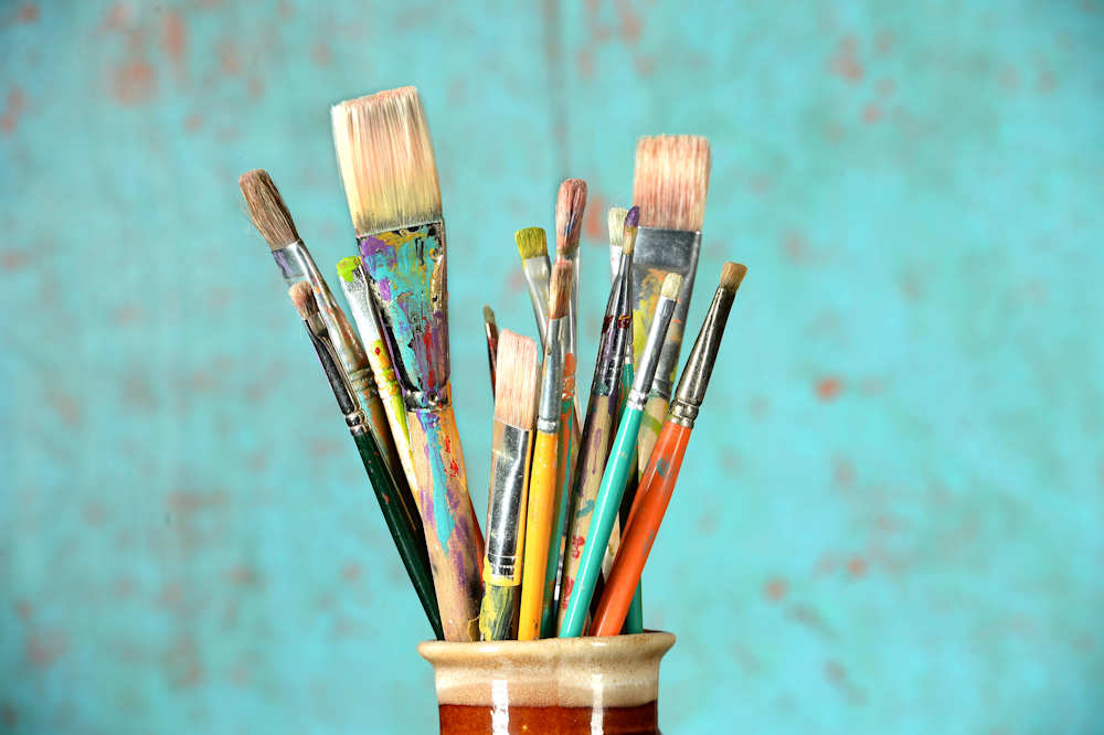 Artist paintbrushes in a jar over colorful background